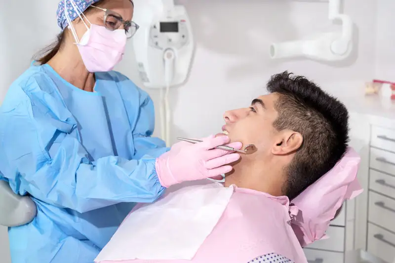 A man sitting in a dentist chair, while the dentist looks at his teeth.