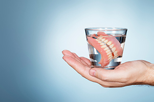 Close up of a hand holding a glass of water with dentures in it at Coulter Family Dentistry in Spokane Valley, WA