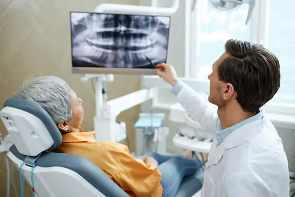 Back view of male dentist pointing at tooth X-ray image on screen during consultation in modern dental clinic at Coulter Family Dentistry in Spokane Valley, WA