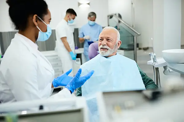 Older patient sitting in dental chair calmly discussing his oral health with his female dentist during dental implant consultation at Coulter Family Dentistry in Spokane Valley, WA